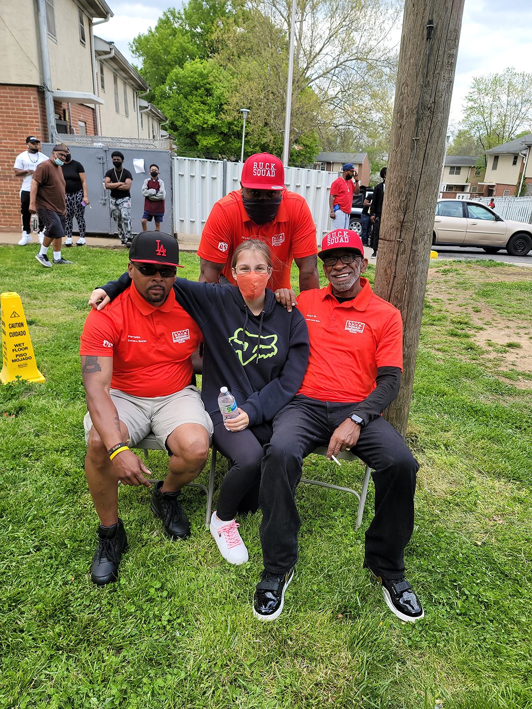 Three members of the BUCK squad sit with an event attendee during a community day at Westhave public housing community