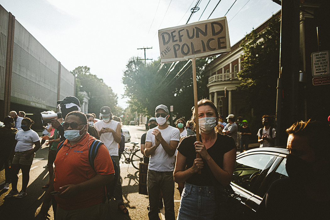 Group of protestors in downtown Charlottesville, one person holds a Defund the Police sign