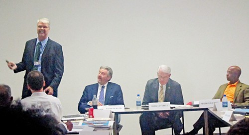 Aitken (standing) at Planning Commission meeting; seated are David Pickler of SCS, Shelby County Mayor Mark Luttrell, and Martavius Jones of MCS.